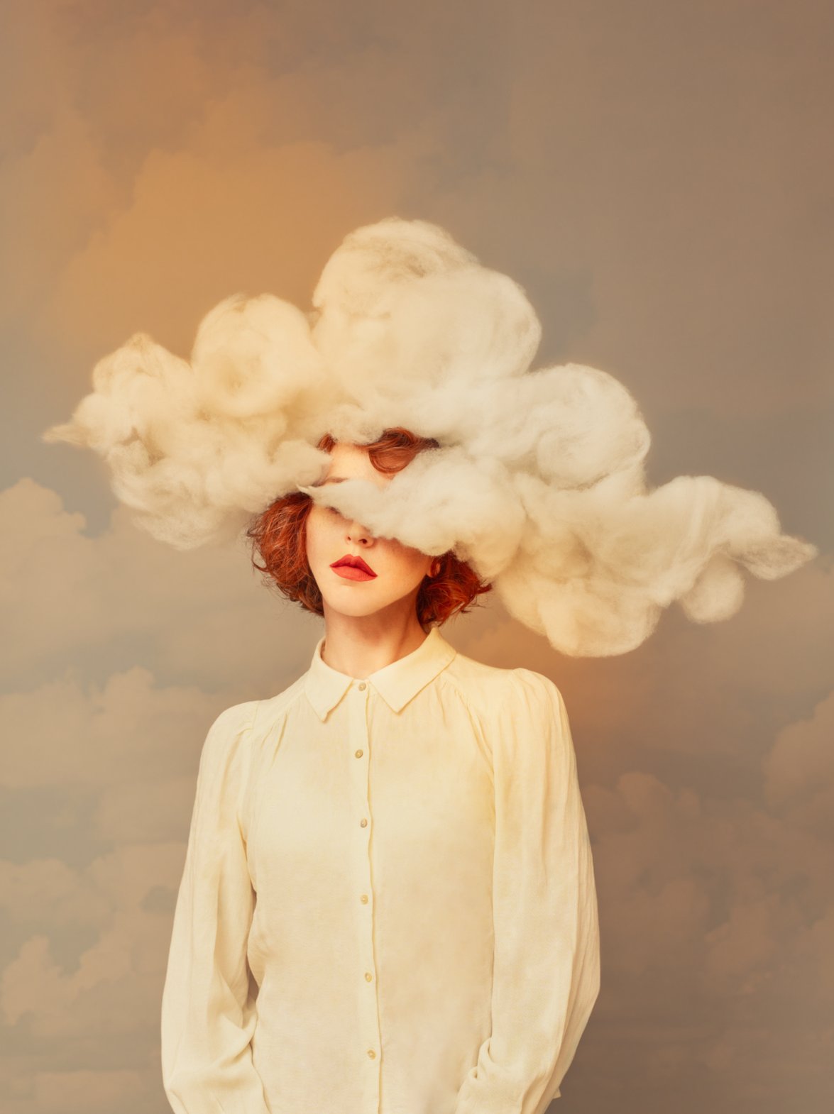 Portrait surréaliste d'une femme rousse au visage caché par un nuage de coton, devant un fond peint de ciel