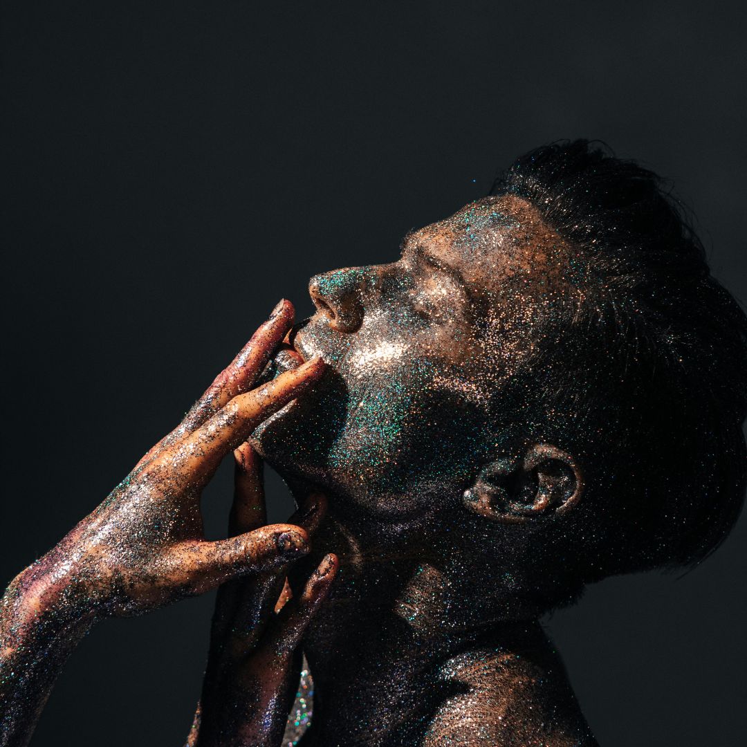 Portrait beauté en studio Linkstar, modèle au visage et aux mains recouverts de paillettes dorées sur fond sombre