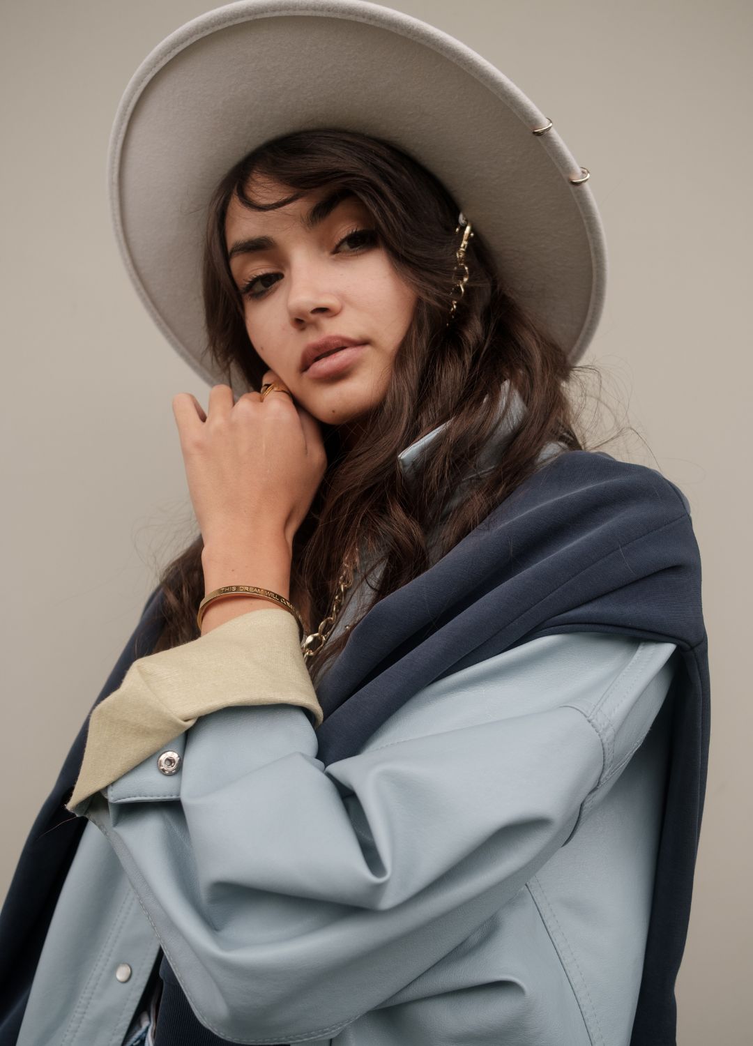 Portrait de mode en studio, modèle au chapeau de feutre clair et veste en cuir bleu sur fond beige