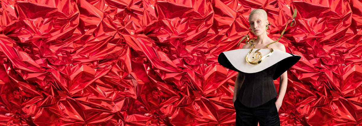 Portrait éditorial devant un fond photo métallique rouge froissé, mannequin en tenue noire et blanche et collier doré