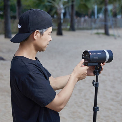 Photographe réglant le flash portable Godox AD300Pro II monté sur un pied à la plage