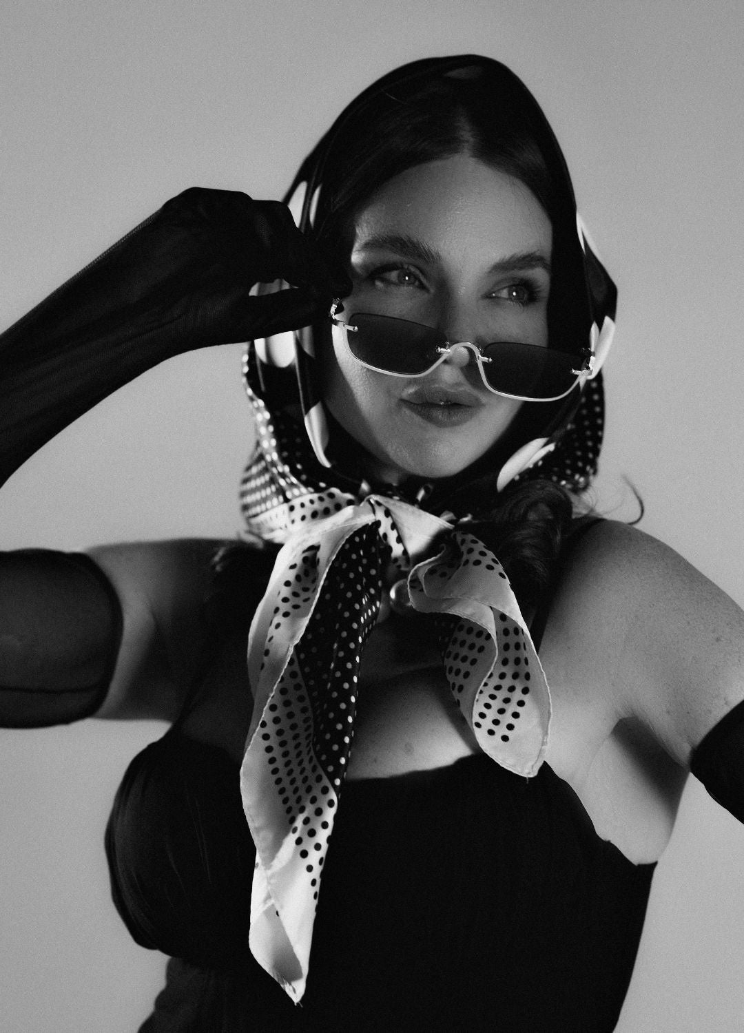 Portrait de mode en studio en noir et blanc, modèle au foulard à pois, lunettes fumées et gants longs sur fond clair