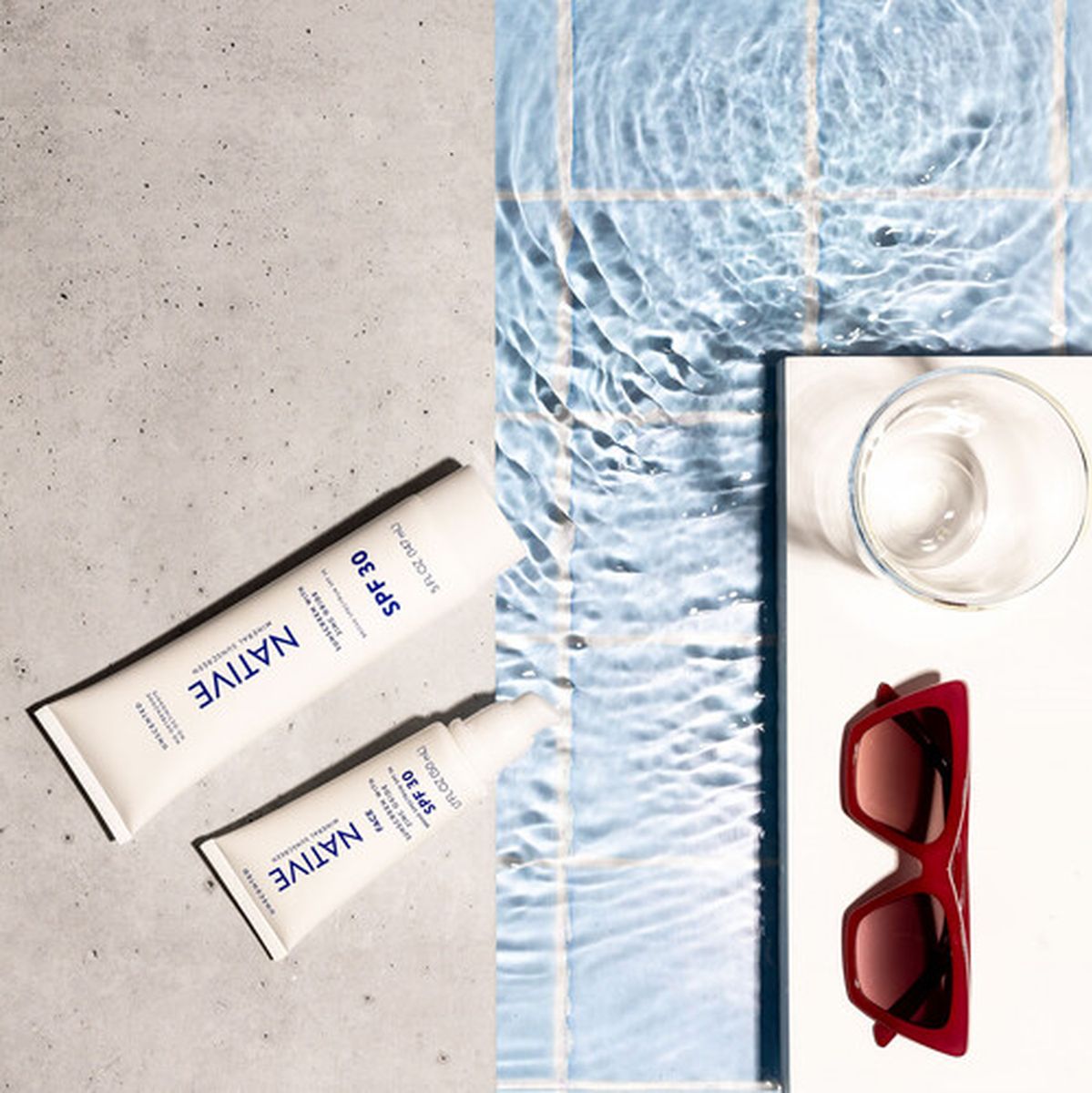 Flat lay réalisé avec l'Aqua Tray, tubes de crème solaire et lunettes au bord d'une surface d'eau