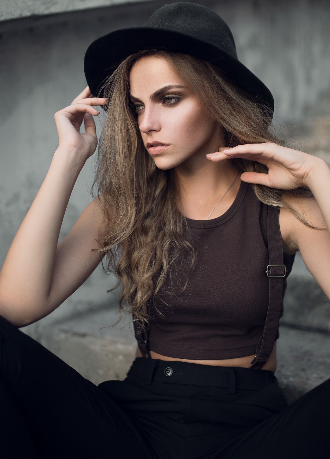 Portrait de mode en extérieur, modèle au chapeau noir à bord large devant un mur de béton